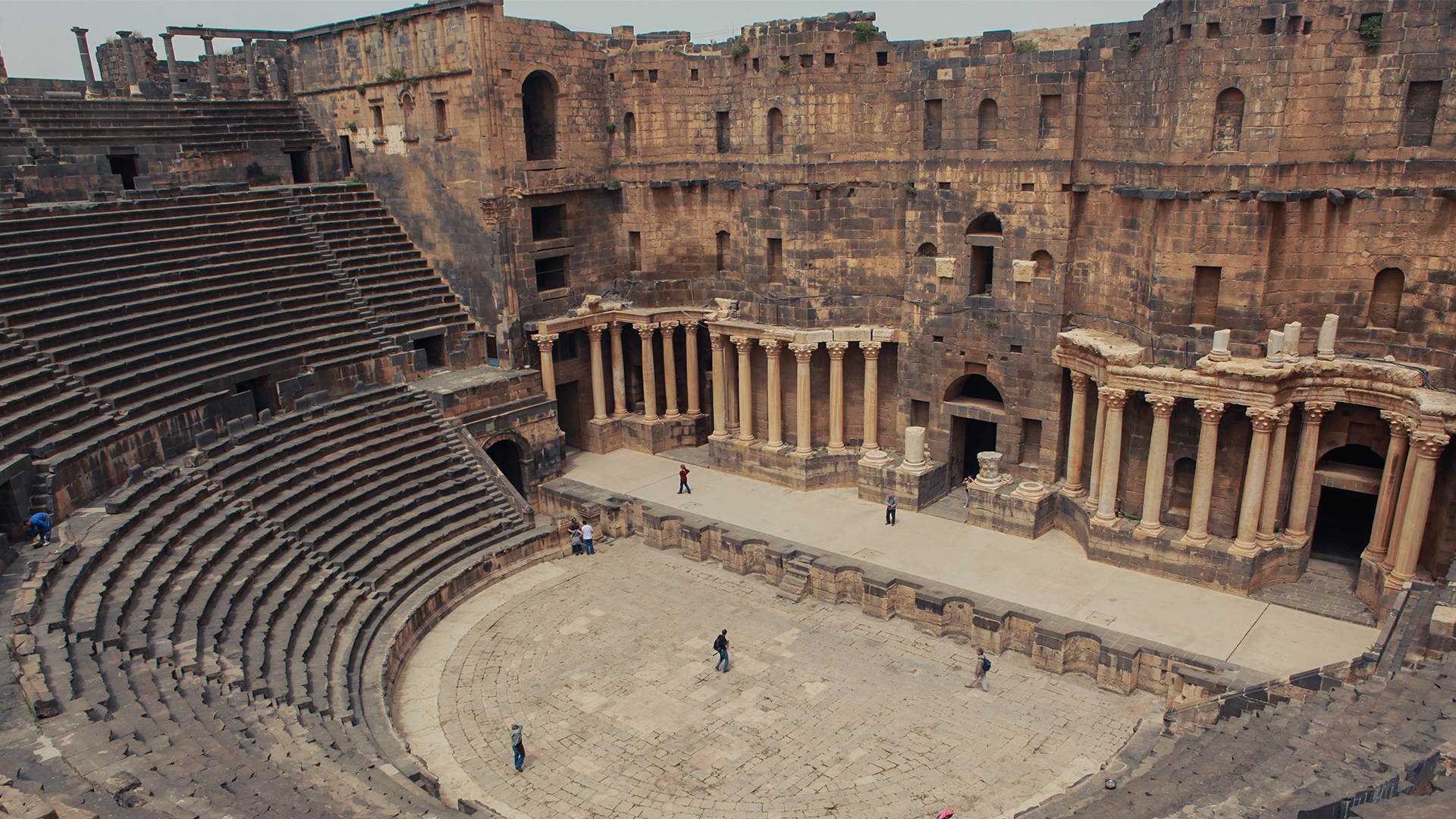 A picturesque view unfolds he Roman Amphitheatre of Bosra, adorned with a scattering of tourists across its grand courtyard.