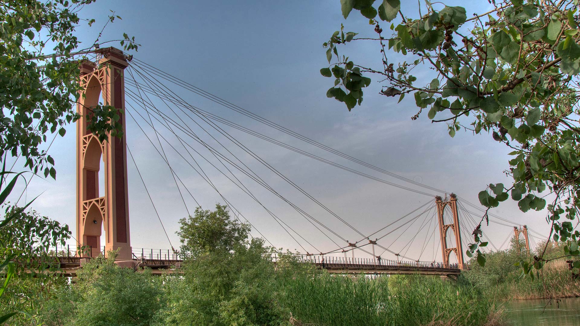 A panoramic photograph captures the iconic pedestrian suspension bridge of Deir EzZor, serving as a symbol of the city, and a testament to architectural ingenuity and urban connectivity.