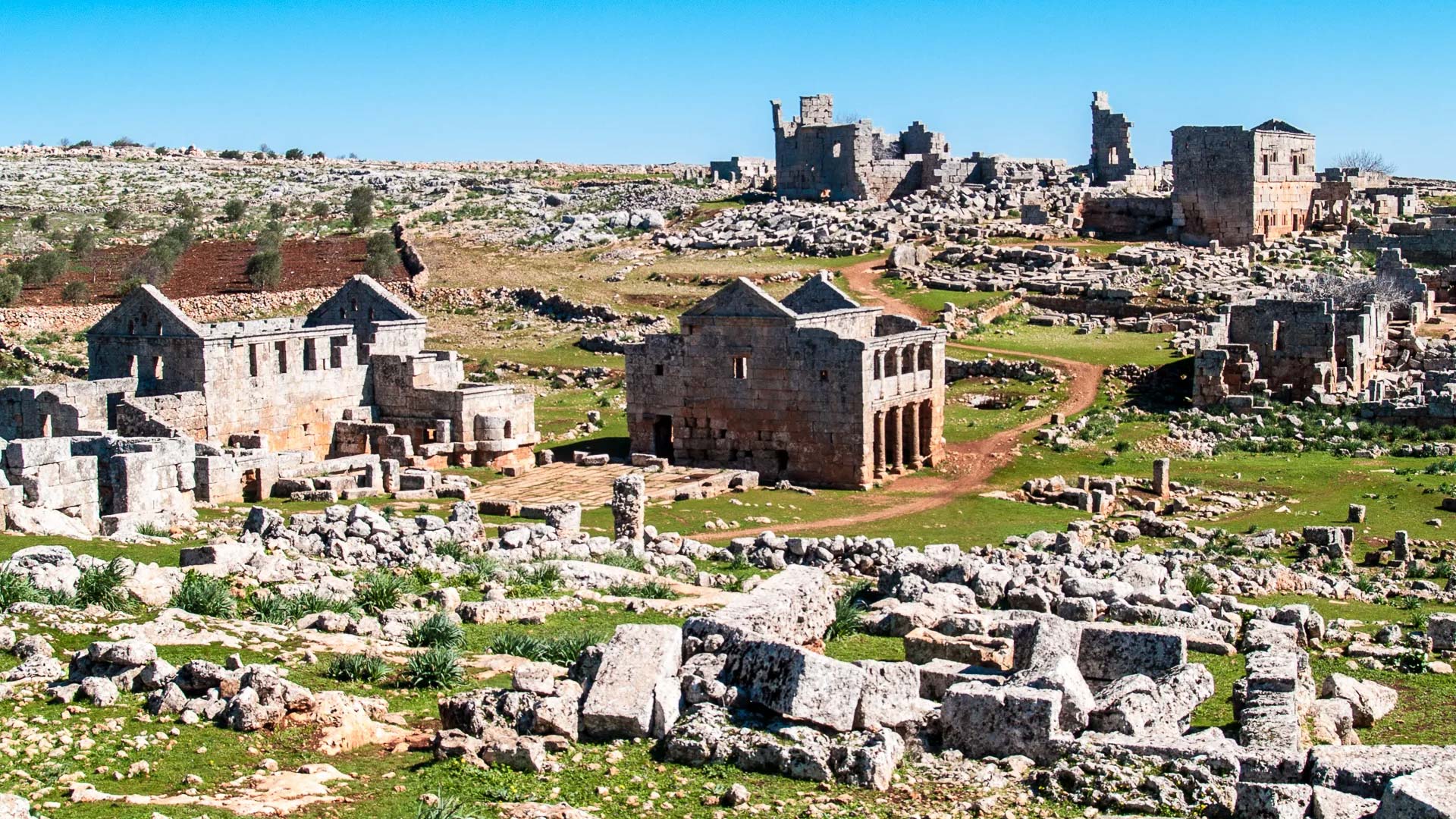 A panoramic photograph captures the sprawling ruins of Serjilla, an archaeological site that encompasses extensive remnants of a fully preserved Byzantine settlement.