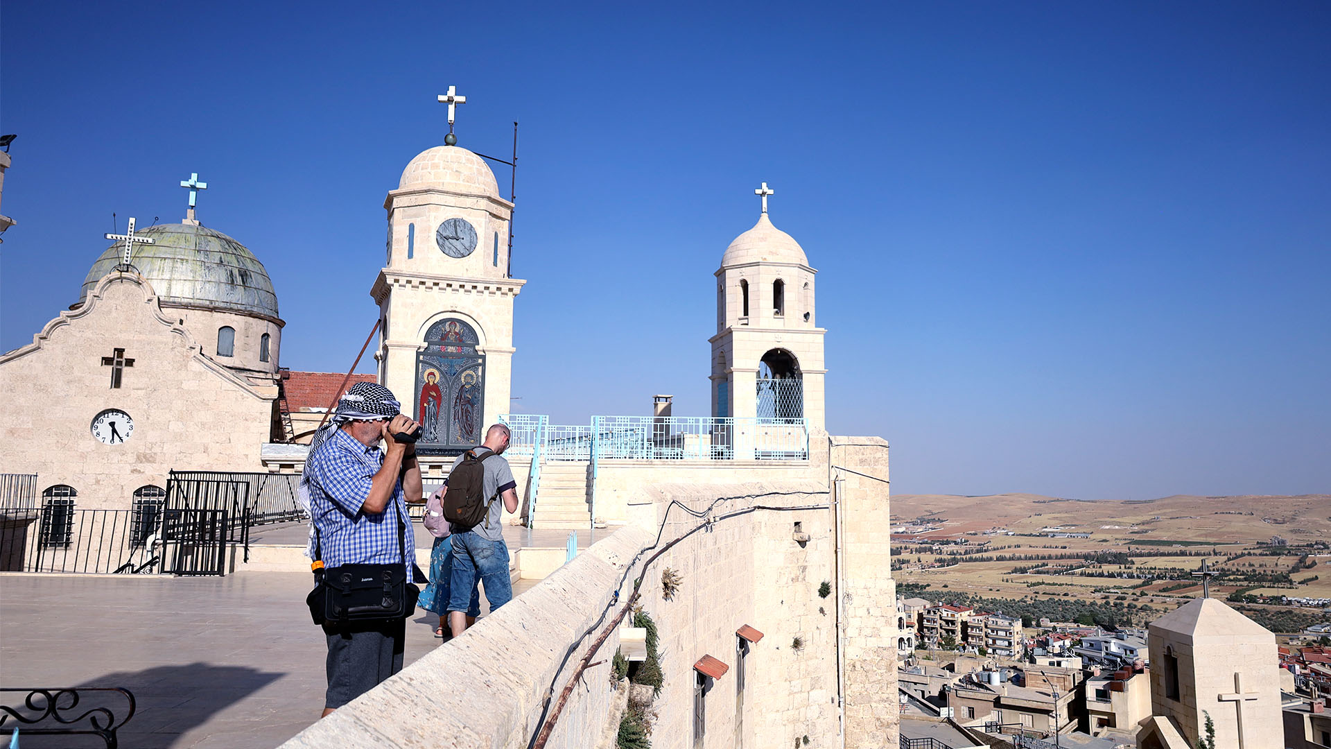 A photograph captures tourists standing on the rooftop of the Convent of Our Lady of Sednaya, enjoying the breathtaking views from the elevated vantage point.
