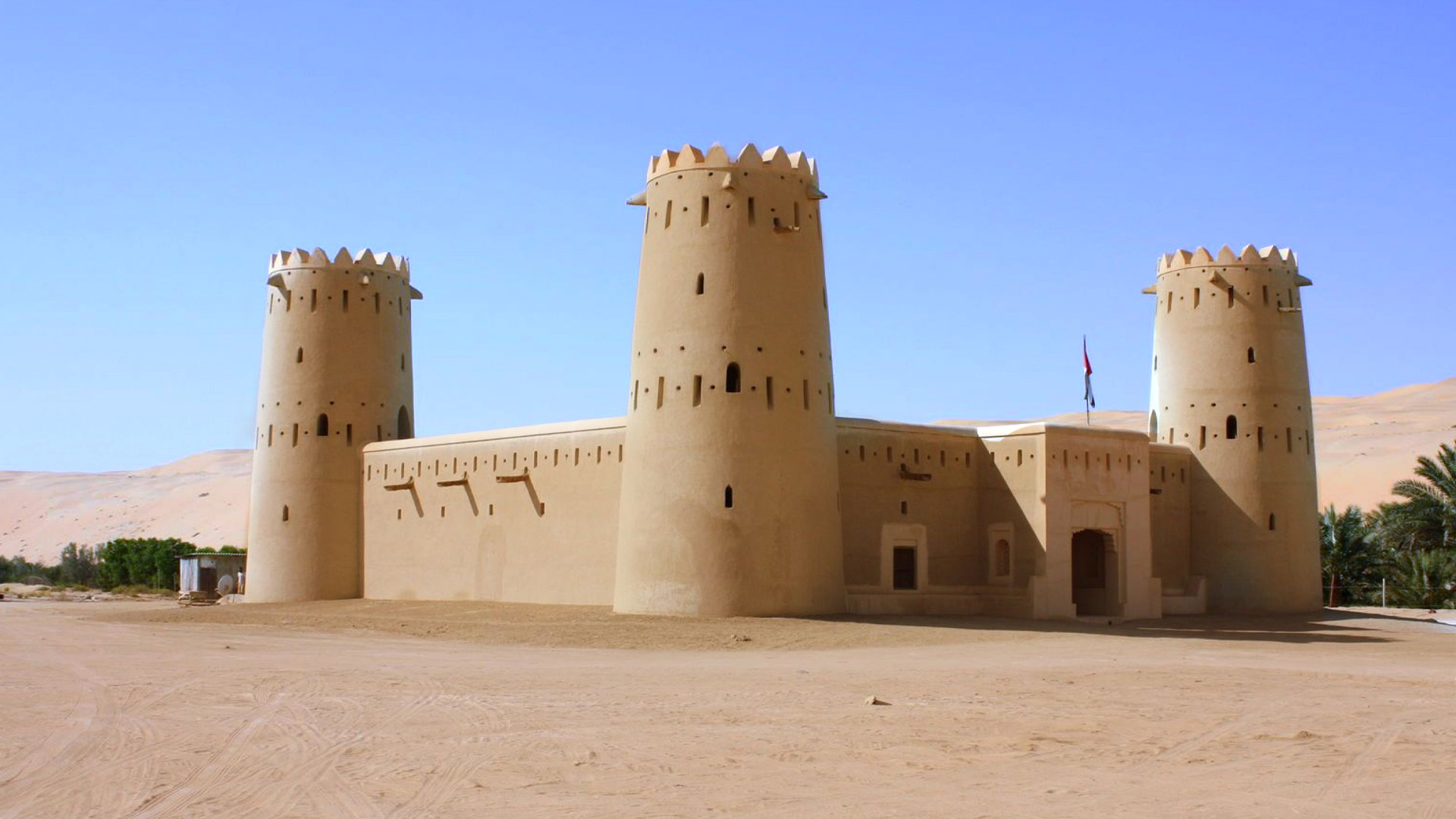 A panoramic photograph immortalizes the square-shaped Qasr Al-Harrana, one of the renowned desert castles, with the backdrop of a clear blue sky.