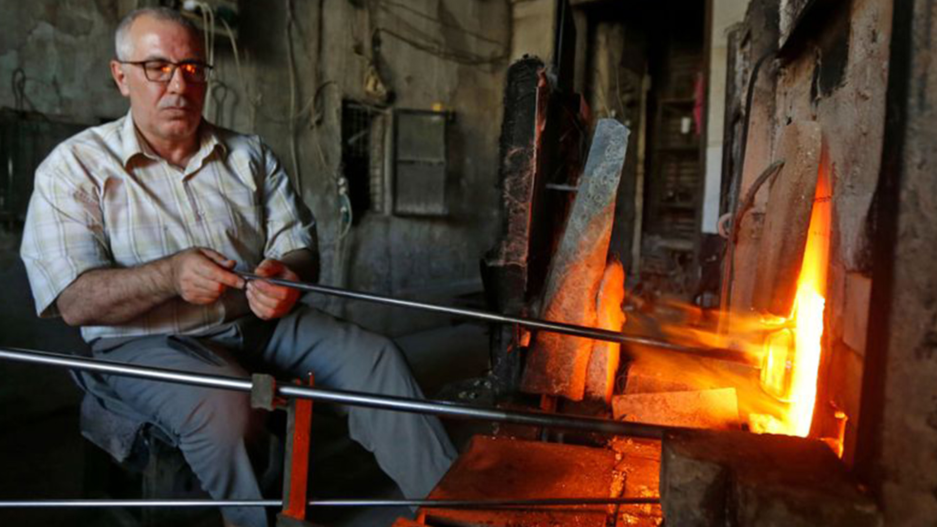 The photograph captures a skilled artisan engrossed in the creation of a remarkable piece of glass art, showcasing the art of glassblowing in Damascus.
