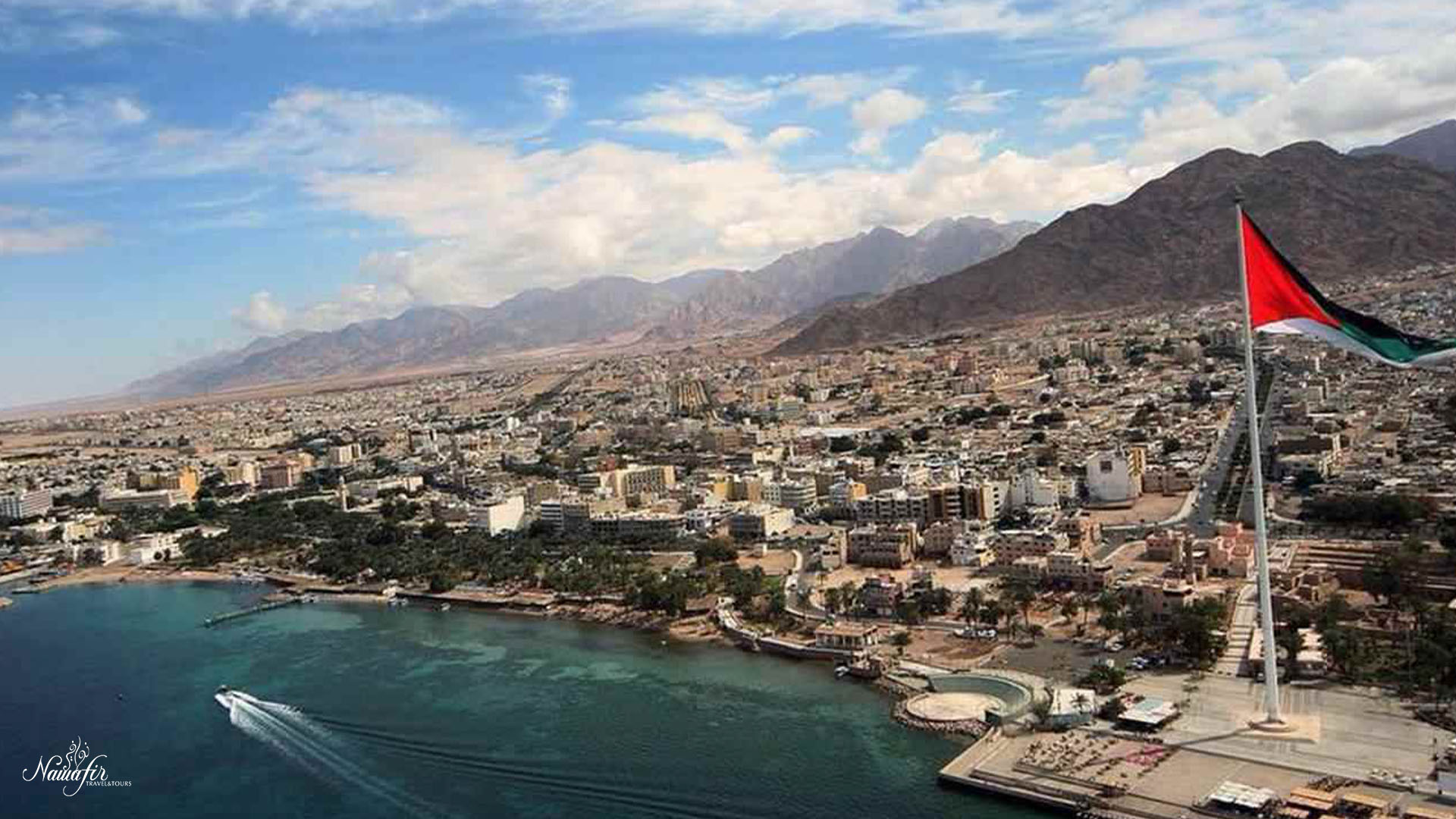 A panoramic photograph immortalizes the coastal city of Aqaba, gracefully adorning the shores of the Red Sea, while buildings and mountains form a striking backdrop.