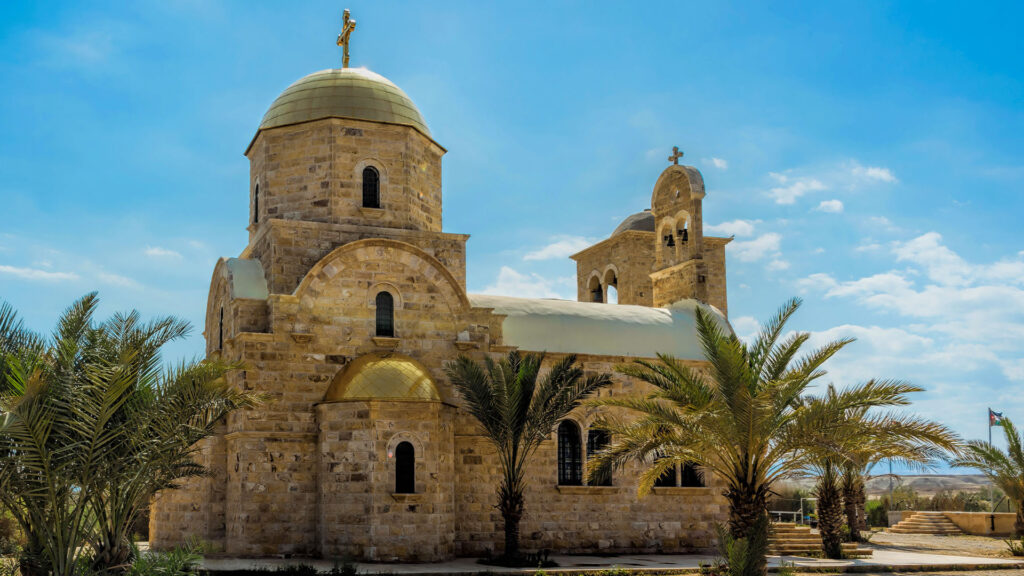 A panoramic photograph captures the timeless essence of the John the Baptist Church of Bethany, enveloped by the presence of elegant palm trees.