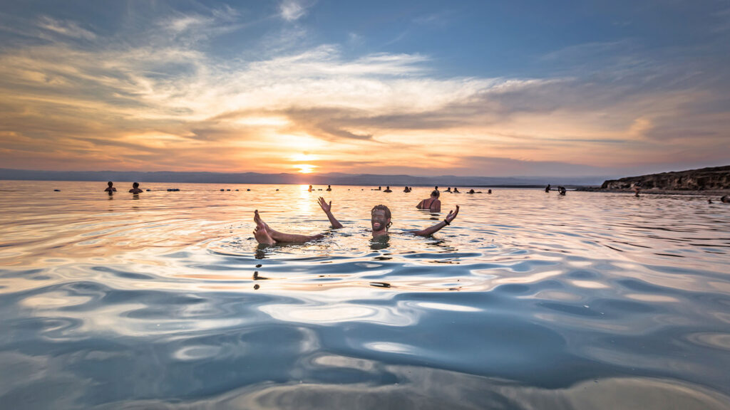 A panoramic photograph immortalizes the captivating sight of a tourist effortlessly floating on the serene waters of the Dead Sea, while swimmers dot the background.