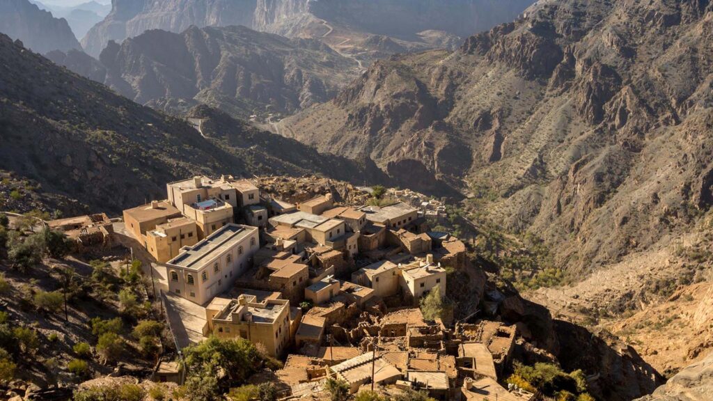 A photograph immortalizes a traditional village nestled in Jebel Akhdar, with towering rugged mountains forming a majestic backdrop.