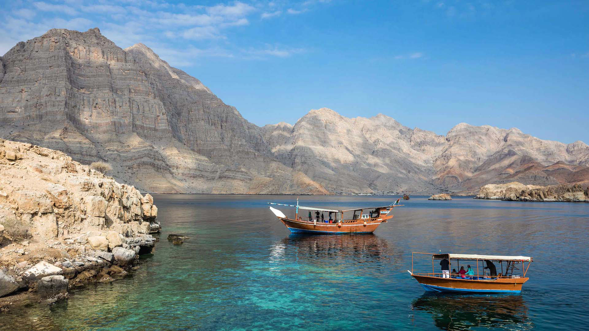 In a panoramic photograph, a sailing boat is immortalized gracefully navigating the waters of the Musandam Peninsula, with the majestic mountains providing a breathtaking backdrop.