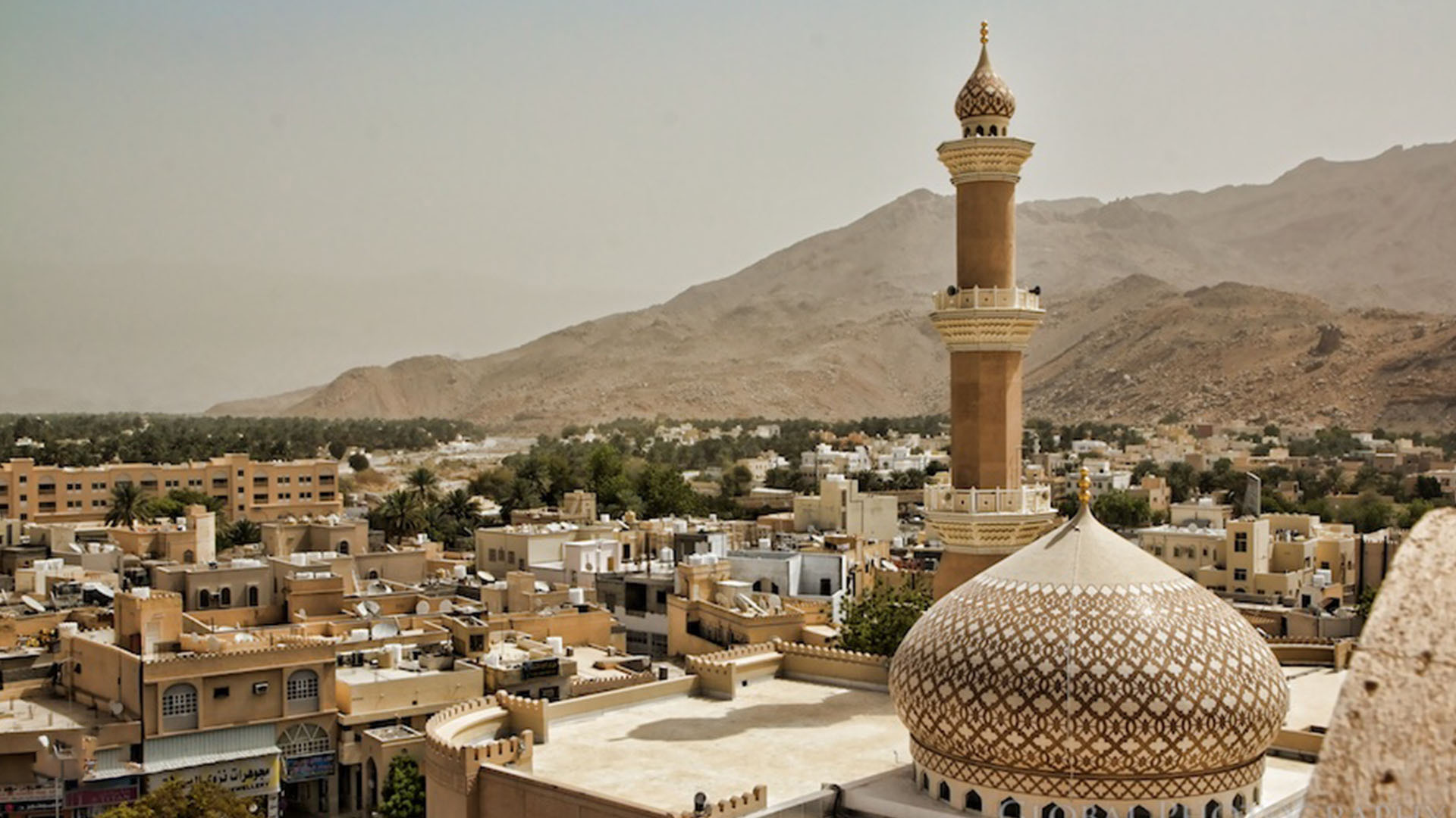 Nizwa: A panoramic photograph captures the majestic Grand Mosque of Nizwa, embraced by a scenic setting of houses and mountains.