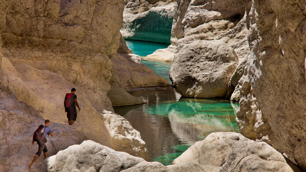 A panoramic photograph immortalizes the captivating Wadi Bani Khalid, where a meandering riverbed winds its way through majestic mountains, crafting a truly awe-inspiring and breathtaking landscape.