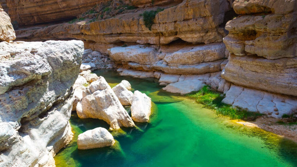 A panoramic photograph captures the enduring allure of Wadi Shab, where a sinuous riverbed carves its way through the rugged mountains.