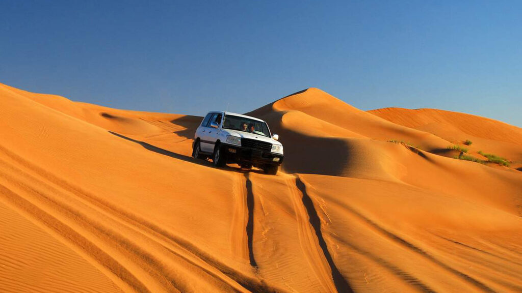 A panoramic photograph captures the unforgettable beauty of Wahiba Sands, where tourists in a 4x4 vehicle traverse the undulating terrain of the remarkable sand dunes.