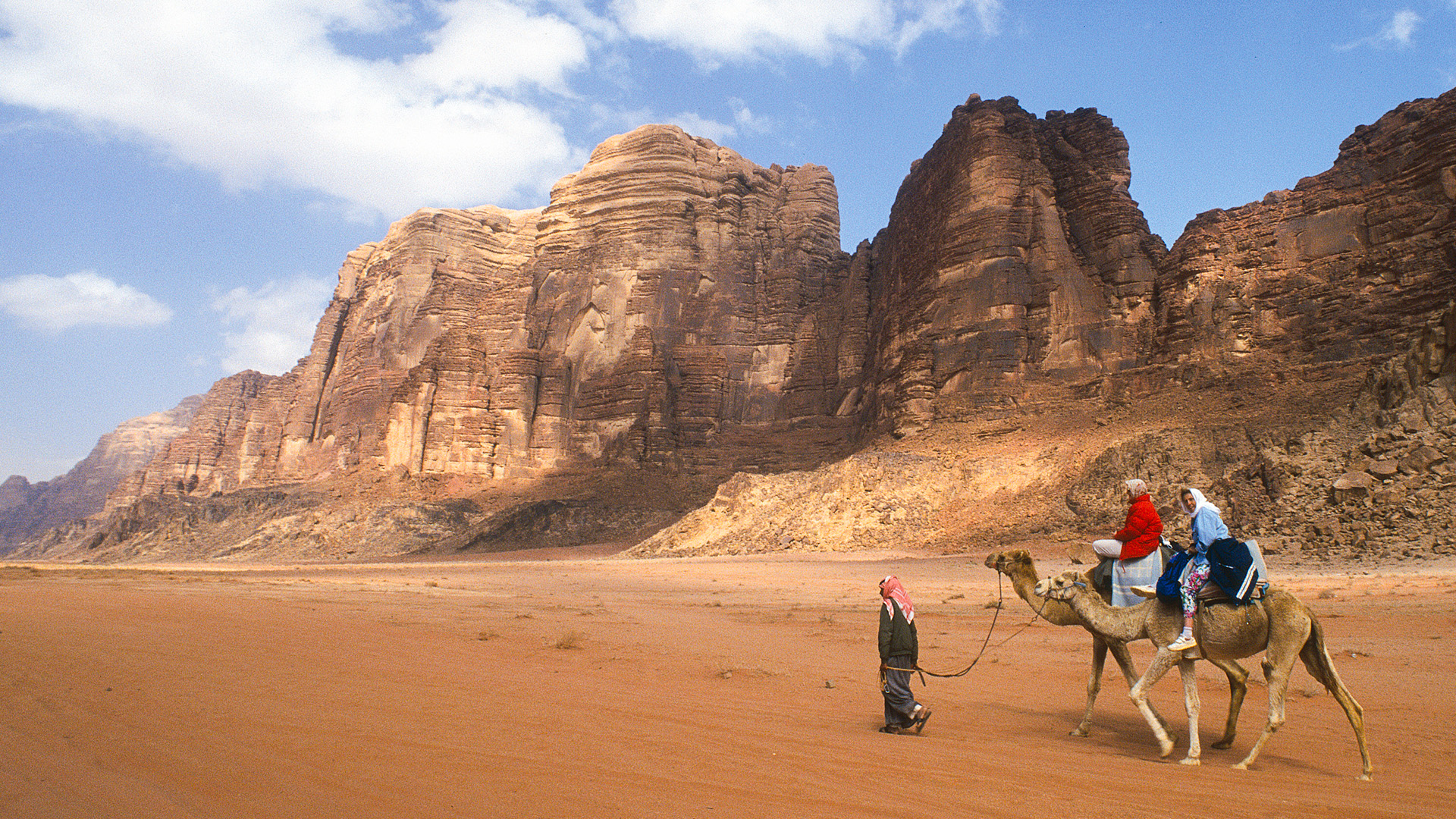 Travel to Jordan: In this panoramic photograph, Wadi Rum is captured, showcasing tourists on camelback against the backdrop of majestic mountains.